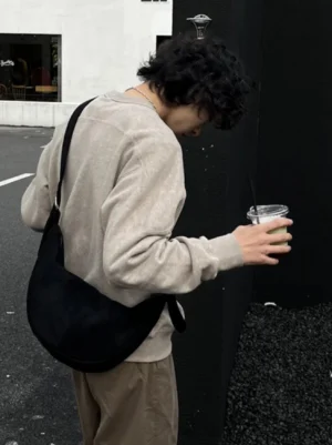 Black matte PU crescent crossbody sling bag worn at the hip from rear view with beige streetwear outfit