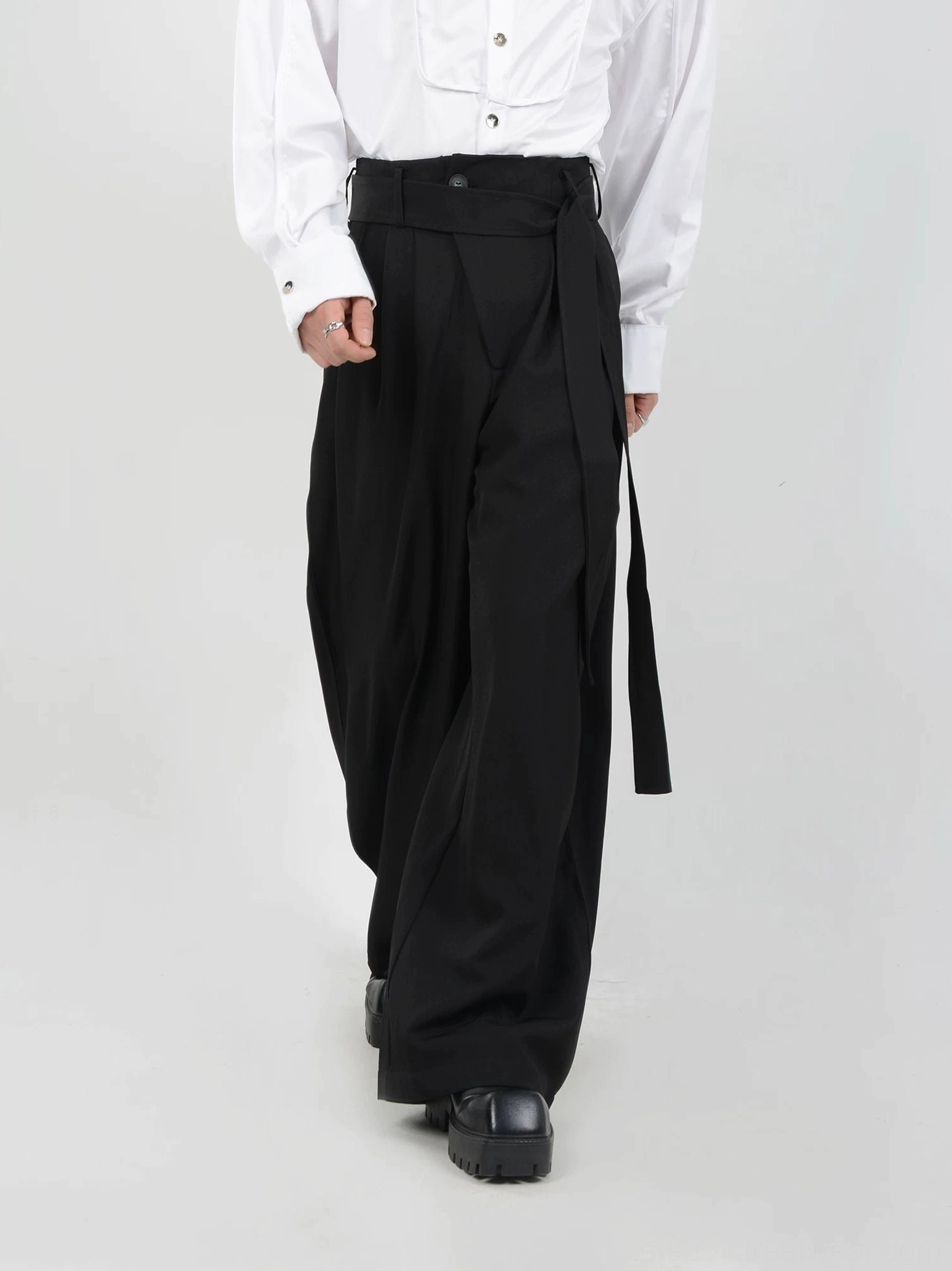 Black high-waisted pleated wide-leg trousers for men rear three-quarter view showing long hanging sash belt