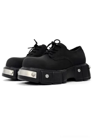Black metal platform Derby shoes in matte finish shown from a front three-quarter view with chunky lug sole, silver metal bolts, front plate details, and classic lace-up closure