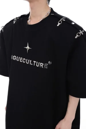 Close-up front view of a black oversized crew neck T-shirt showing reflective silver metallic logo lettering, star decoration, and utility-inspired shoulder buckles