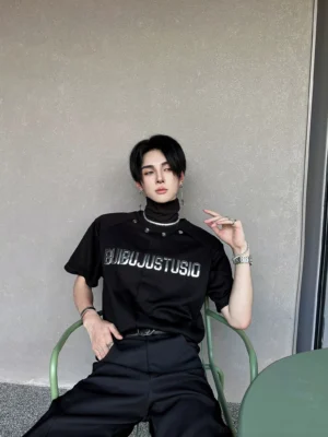 Front three-quarter view of a black Korean streetwear graphic T-shirt with metallic silver chest lettering and industrial studded snap collar