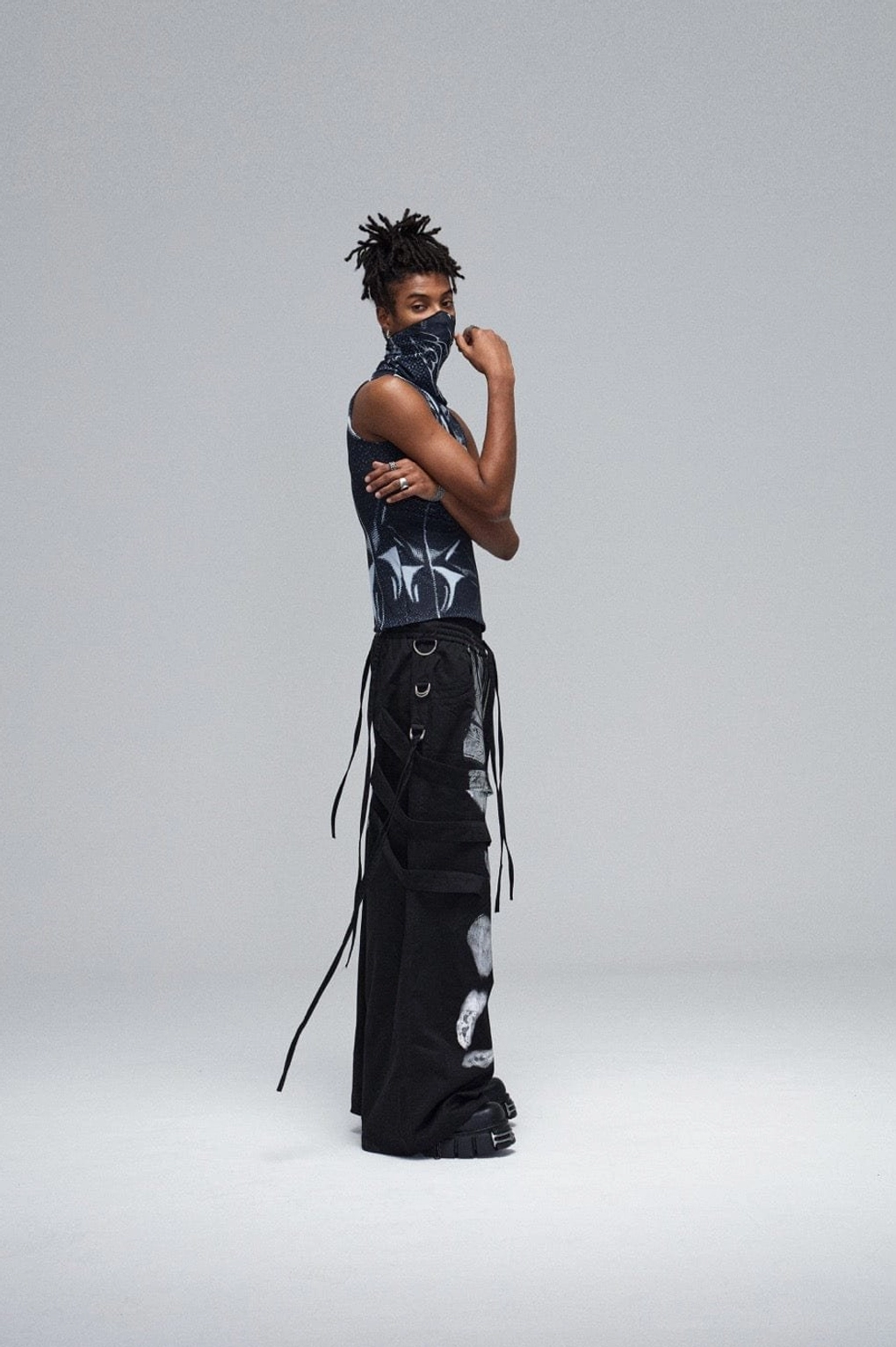 Back three-quarter view of black metallic strap graffiti cargo pants with long side drawstrings, rear strap details, and oversized fit