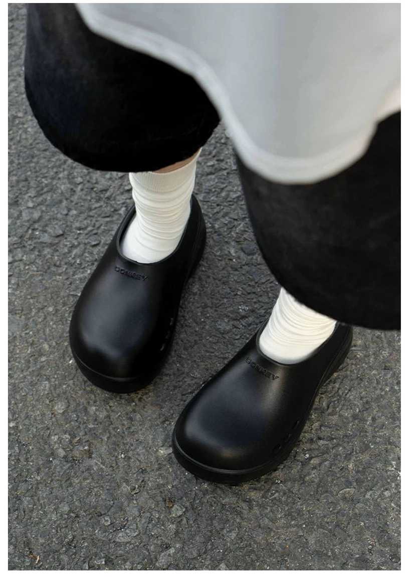 Black Midnight Wave platform clogs worn with white crew socks, cropped black pants and casual streetwear outfit on an outdoor city pavement