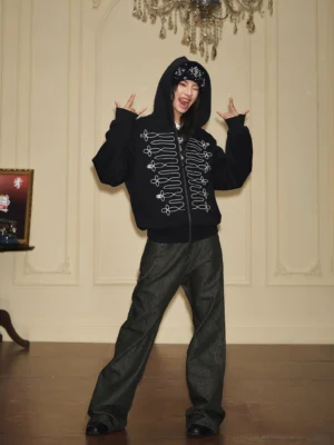 Full-body front view of a relaxed black military embroidered zip-up hoodie with bold white front embroidery in a vintage indoor fashion setting