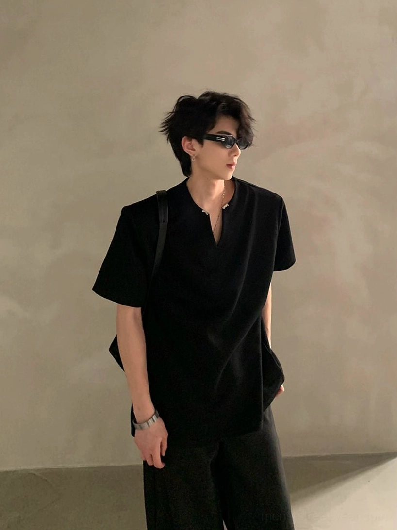 Male model in a solid black minimalist V-neck notch shirt styled with wide-leg trousers and shoulder bag for understated Korean fashion