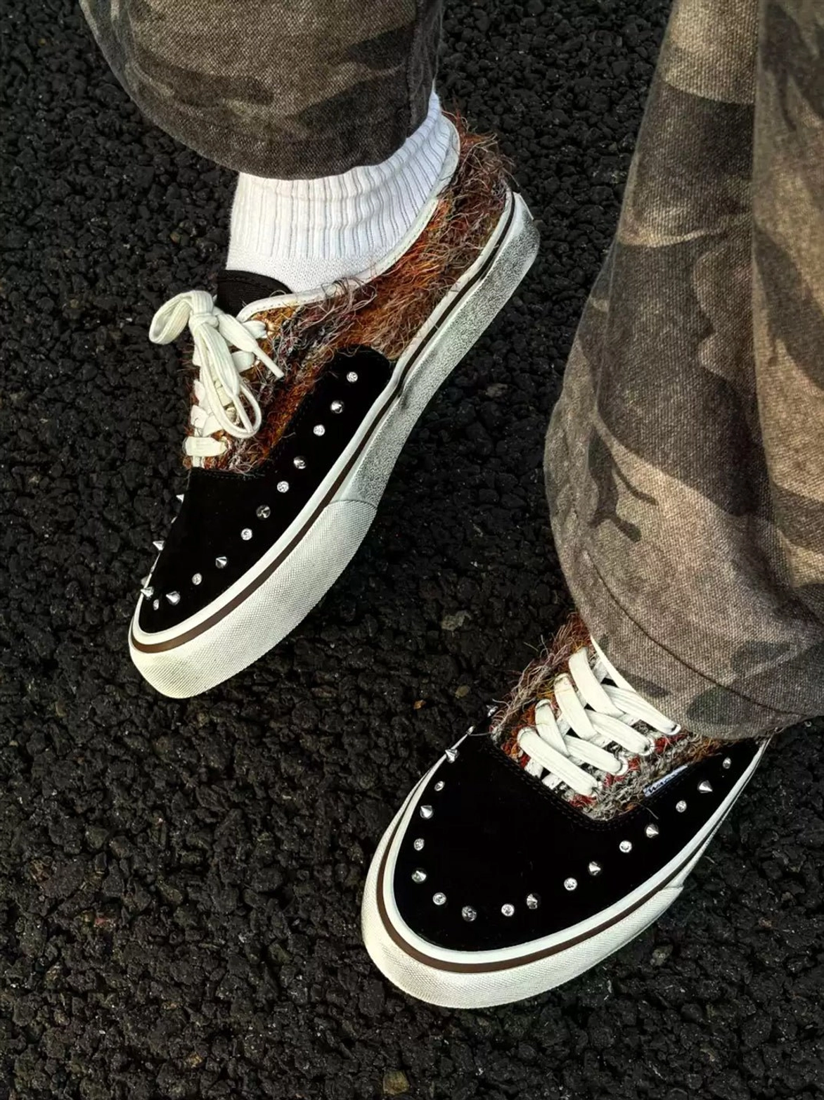 Side view of black mohair-panel studded sneakers worn with camouflage pants, highlighting silver rivets, fuzzy panels, and distressed white midsoles