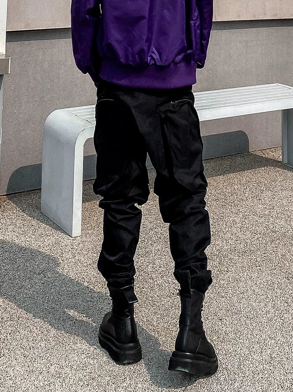 Back view of black multi-pocket cargo jogger pants showing rear utility pockets, durable matte fabric, tapered legs, and elasticized ankle cuffs