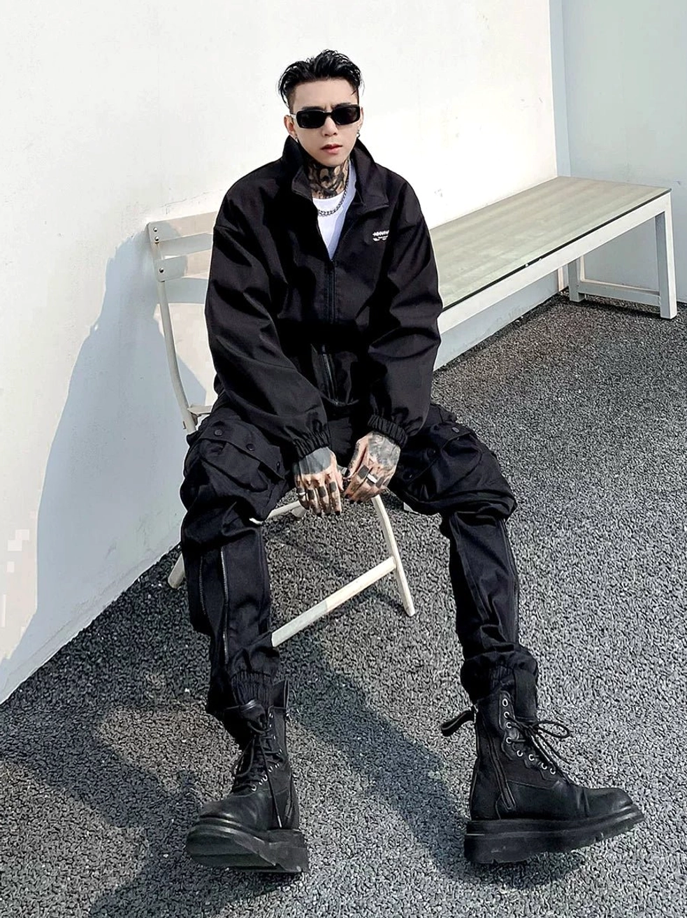 Black multi-pocket combat cargo jogger pants in a seated front view, showing tapered elastic cuffs, layered utility pockets, and matte streetwear fabric