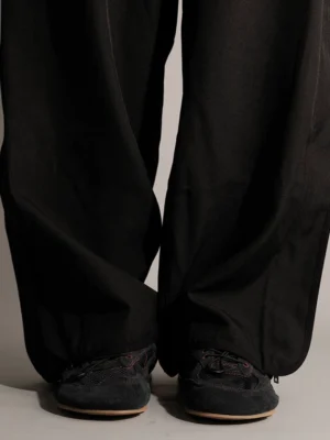 Model wearing black nubuck low-profile streetwear trainers with tan gum soles and wide-leg black trousers