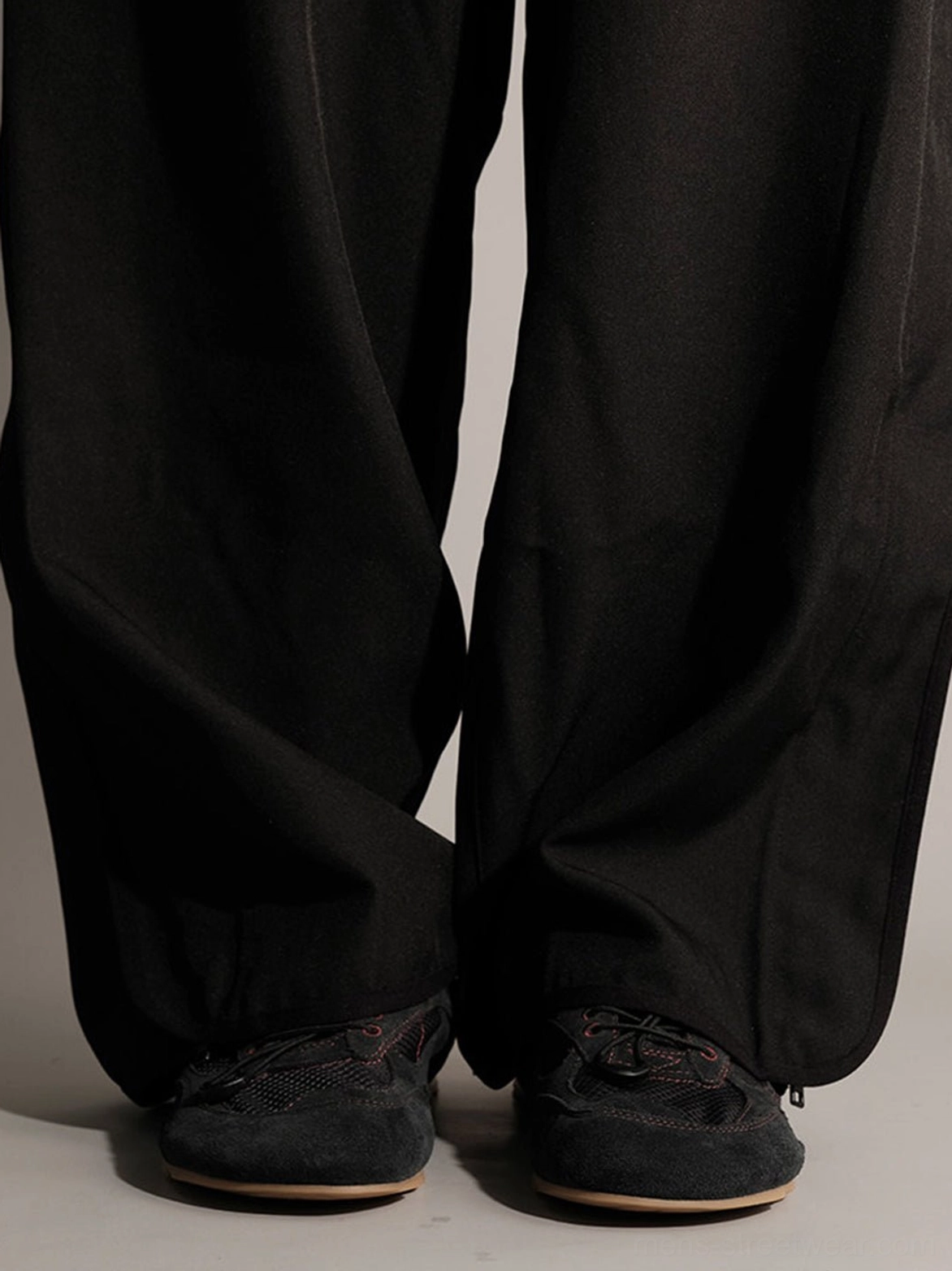 Model wearing black nubuck low-profile streetwear trainers with tan gum soles and wide-leg black trousers