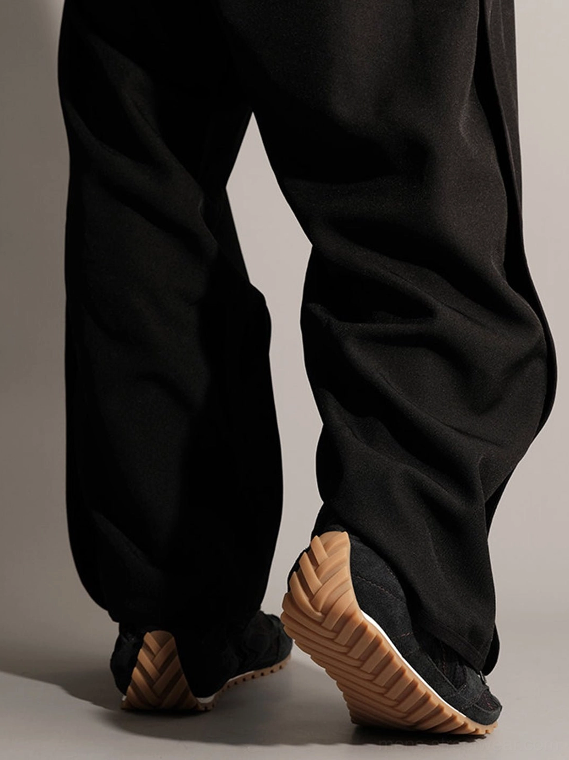 Rear view of black nubuck low-profile trainers showing textured tan gum rubber outsole and heel construction