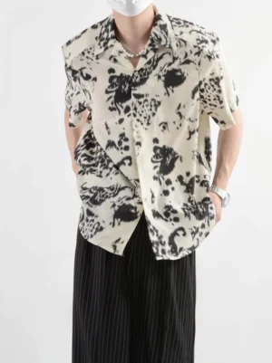 Front view of a male model wearing a black and off-white abstract ink print short-sleeve shirt with relaxed Korean streetwear styling and wide-leg pinstriped trousers
