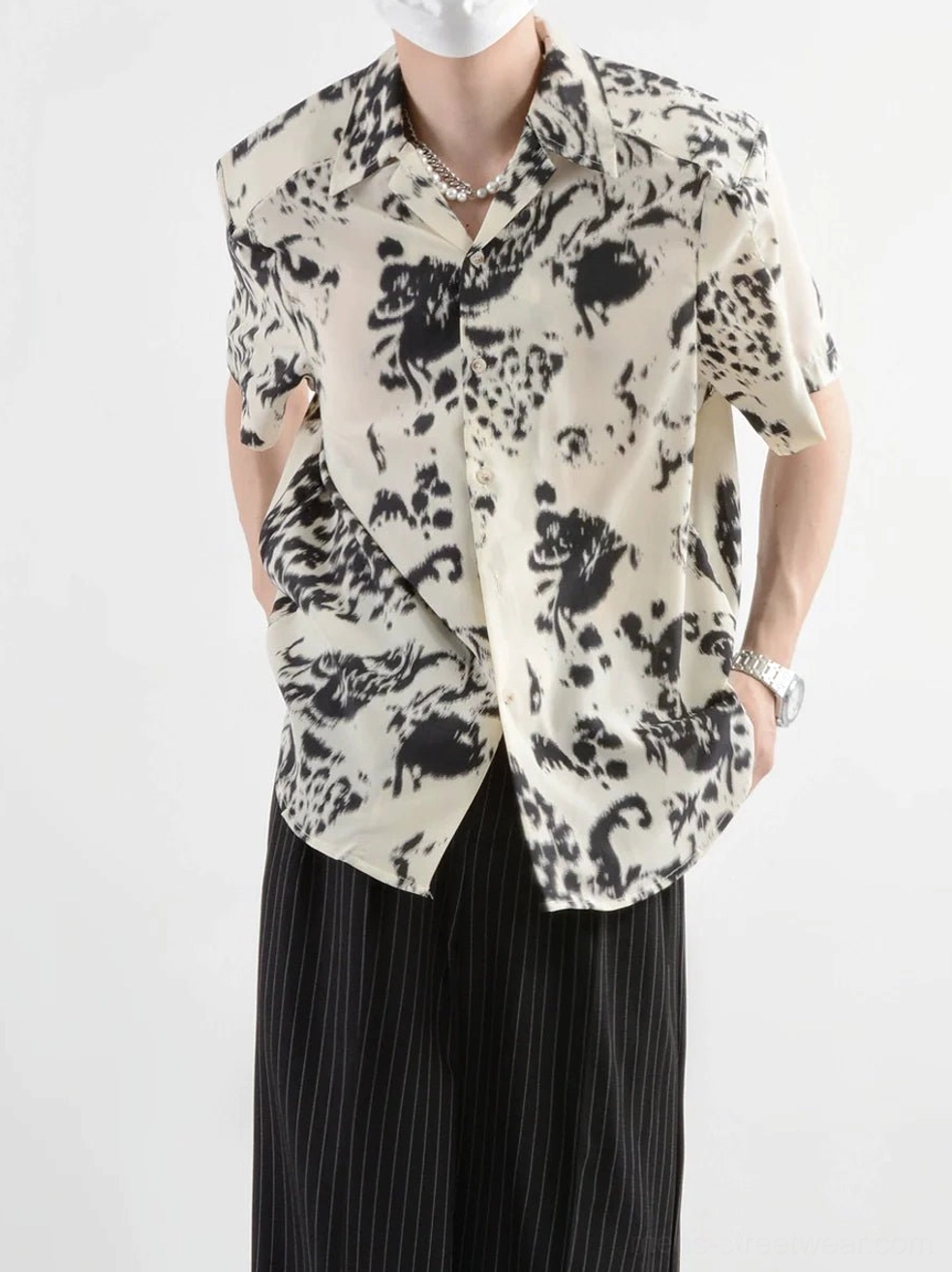 Front view of a male model wearing a black and off-white abstract ink print short-sleeve shirt with relaxed Korean streetwear styling and wide-leg pinstriped trousers