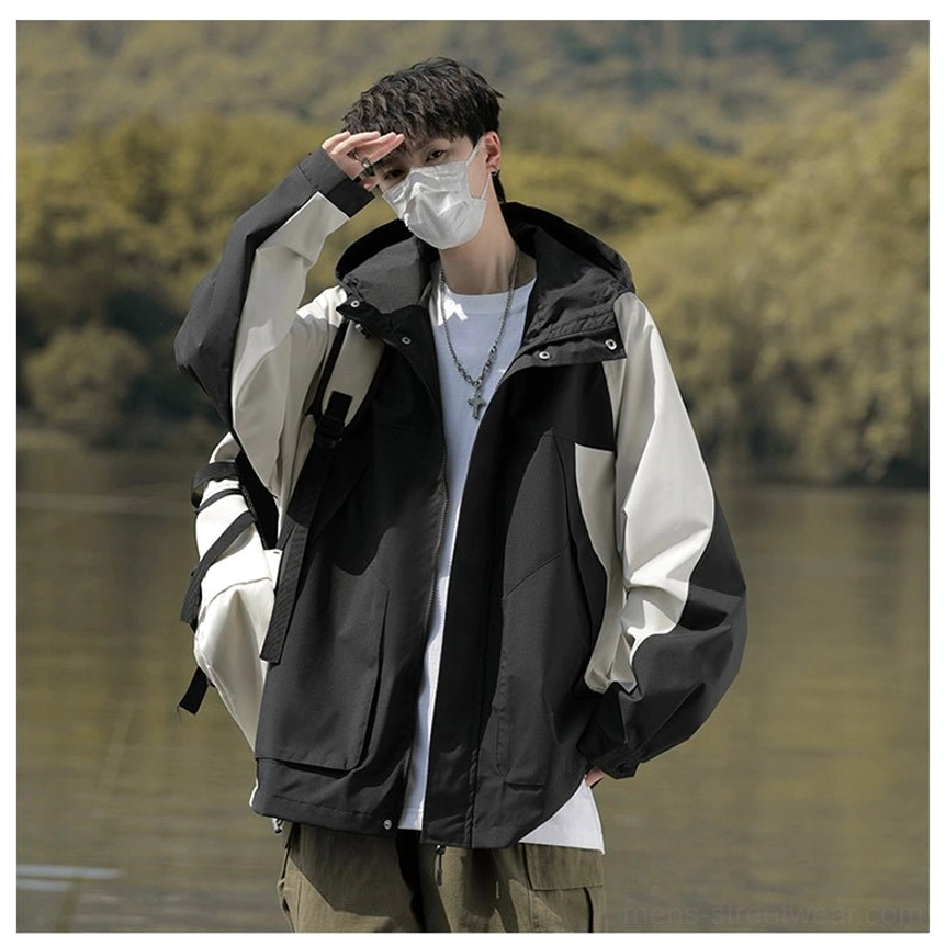 Male model styling a black and off-white colorblock hooded windbreaker jacket with cargo trousers