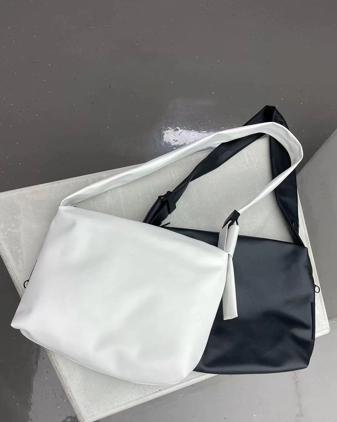 Black and off-white minimalist PU leather tech sling bags flat lay showing soft matte finish and tassel zipper pulls
