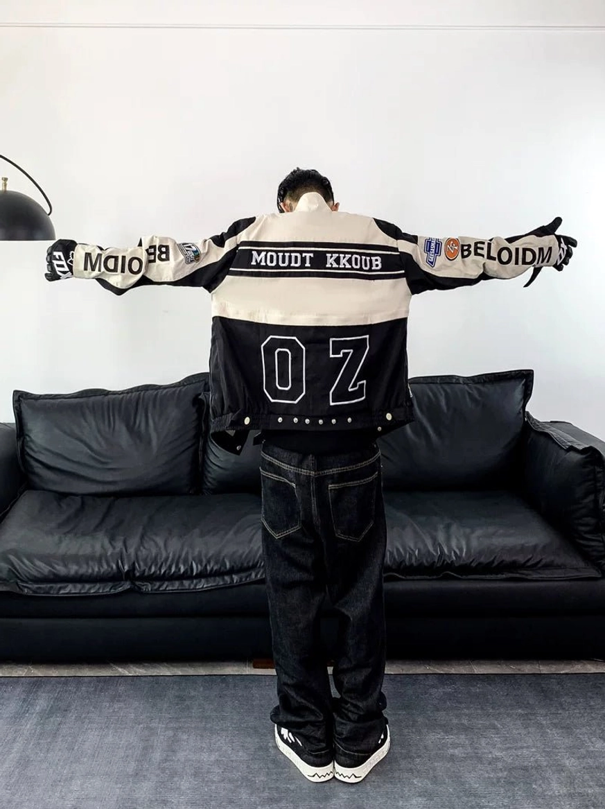Back view of a black and off-white motorcycle racing varsity jacket with large racing graphics, sleeve patches, dark jeans, and sneakers