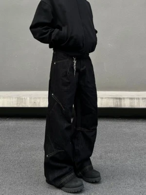 Three-quarter front view of black deconstructed wide-leg jeans with asymmetric panel stitching and stacked hem