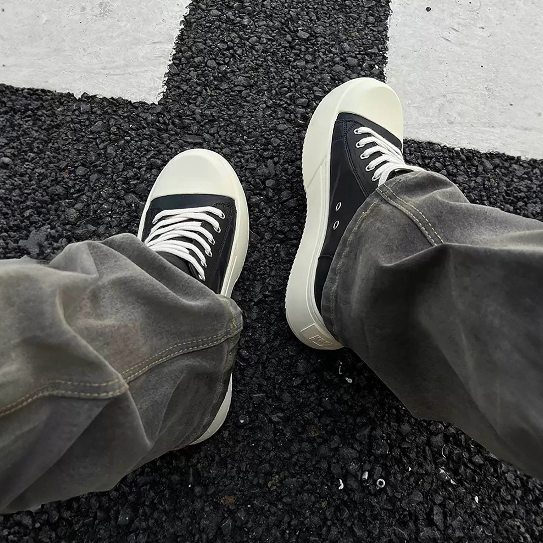 Top-down on-foot view of Black Oreo low-top platform streetwear sneakers with gray jeans on a crosswalk