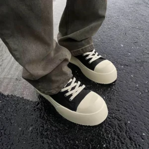 Black Oreo low-top platform streetwear sneakers worn with gray jeans on wet city pavement side view