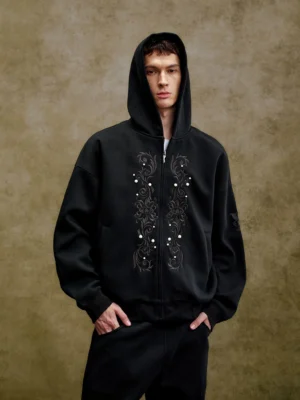 Black ornate pearl embroidered boxy zip-up hoodie shown on male model with oversized streetwear fit and front scrollwork