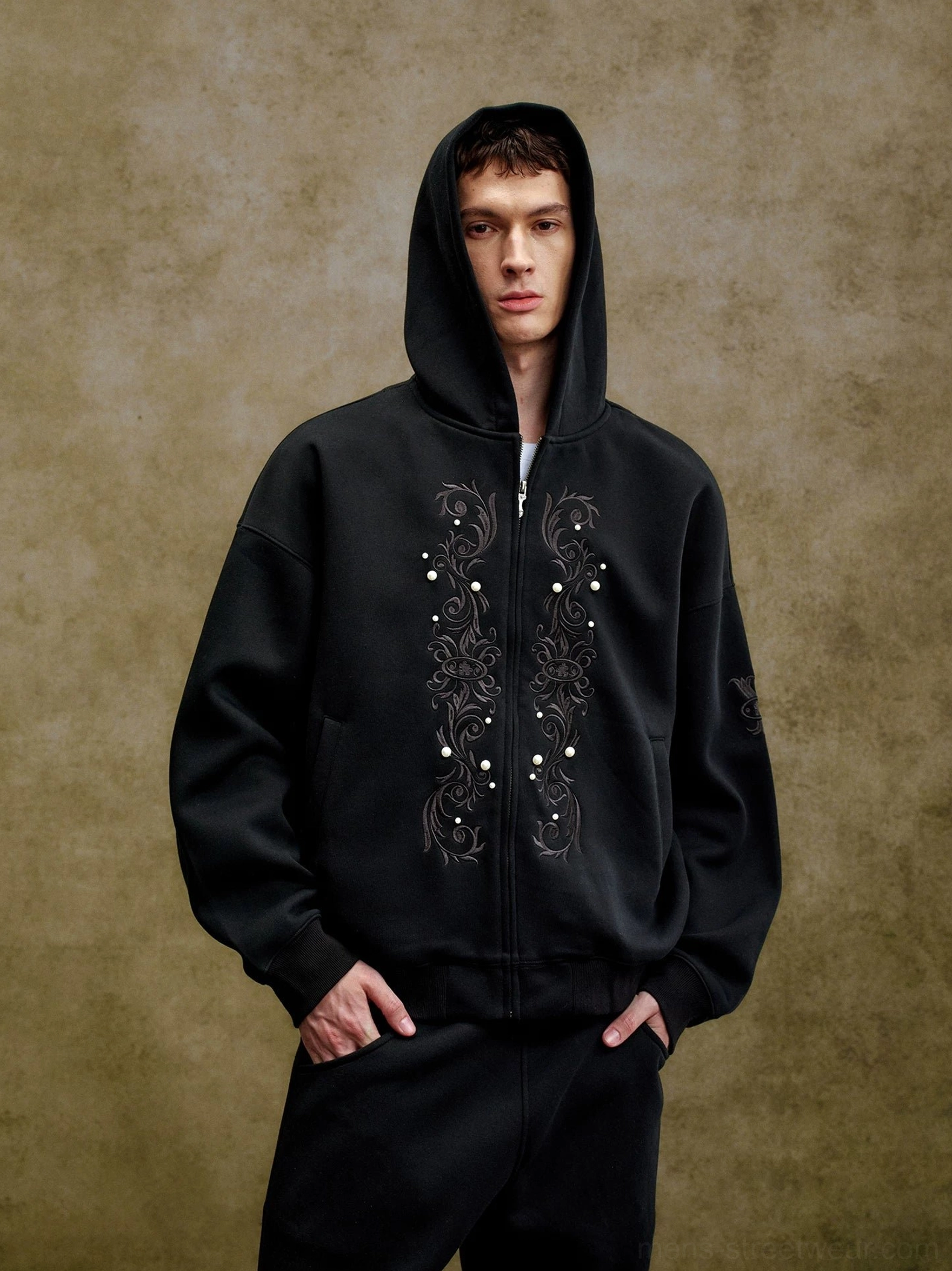 Black ornate pearl embroidered boxy zip-up hoodie shown on male model with oversized streetwear fit and front scrollwork