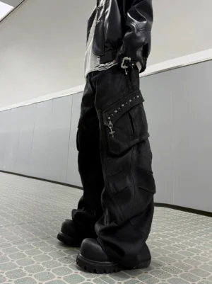 Side view of oversized black cargo pants with studded side pocket trim, metal clasp details, and dramatic wide-leg streetwear silhouette