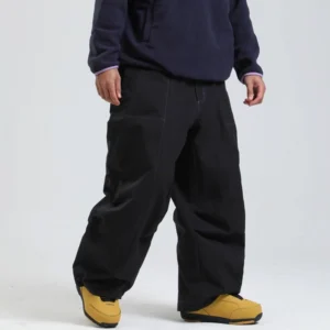 Black oversized cargo snow pants shown from the front three-quarter view with contrast stitching, multiple pockets, relaxed wide legs, and yellow snow boots