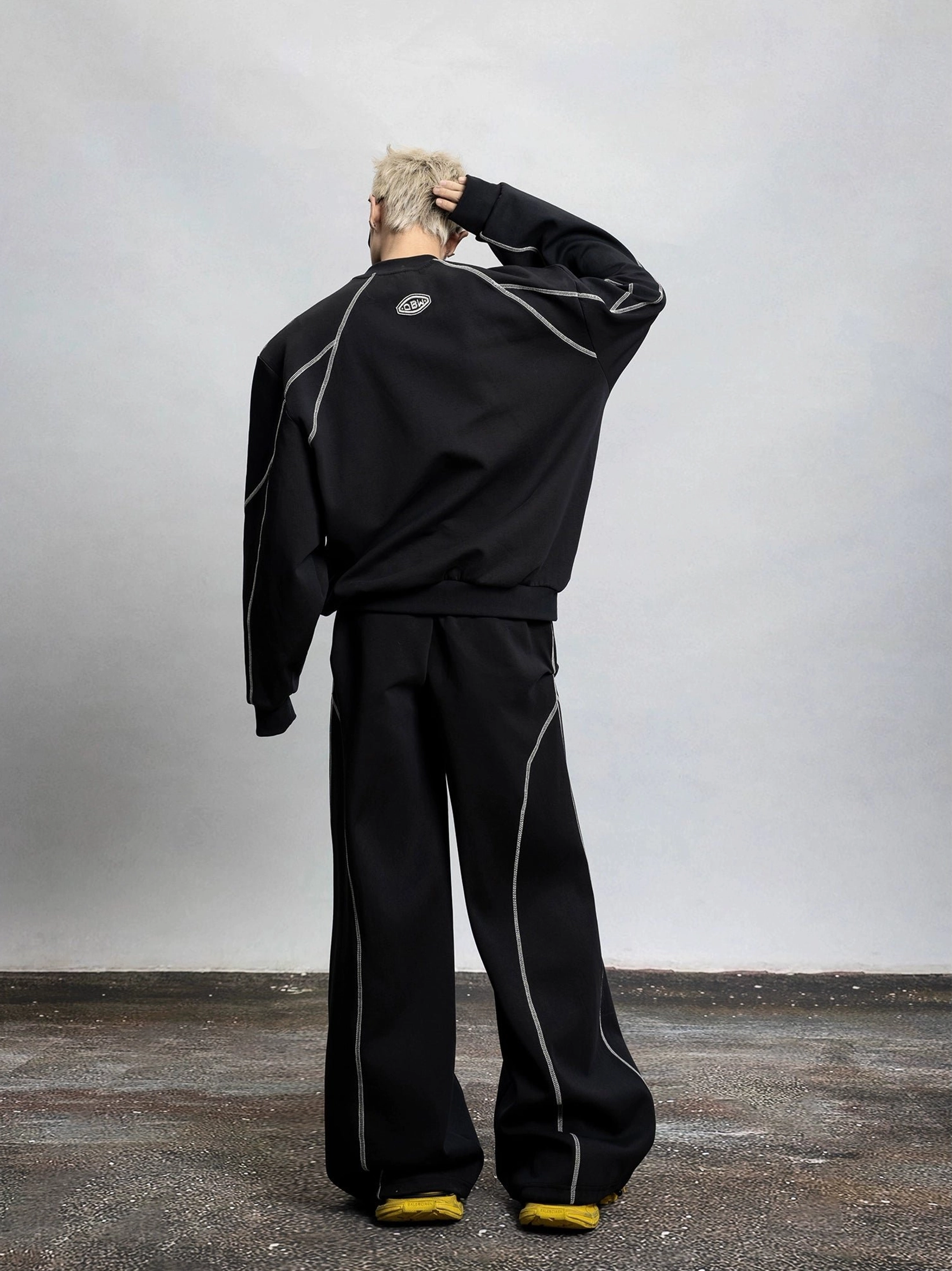 Full back view of a black oversized contrast stitch sweatshirt with silver topstitching, upper back embroidery, and relaxed dropped shoulder fit