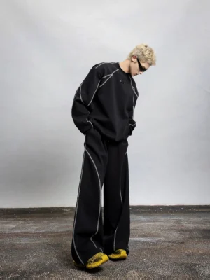 Full body side view of a black oversized contrast stitch sweatshirt with detachable shoulder pads styled with matching wide leg trousers in a modern streetwear outfit