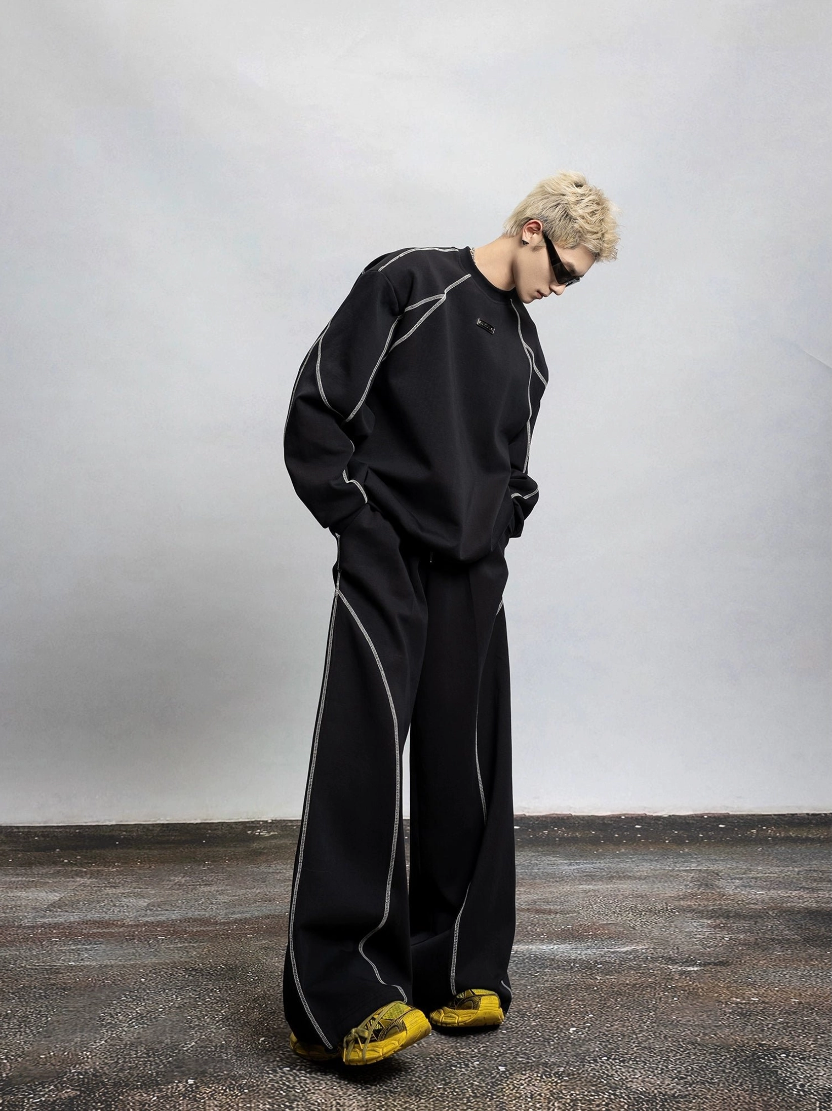 Full body side view of a black oversized contrast stitch sweatshirt with detachable shoulder pads styled with matching wide leg trousers in a modern streetwear outfit