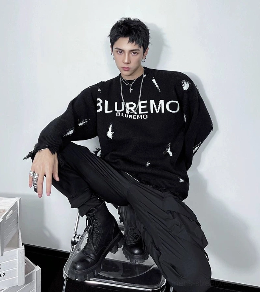 Three-quarter front view of a black oversized distressed knit sweater with graphic chest lettering, frayed holes, cargo pants, and combat boots