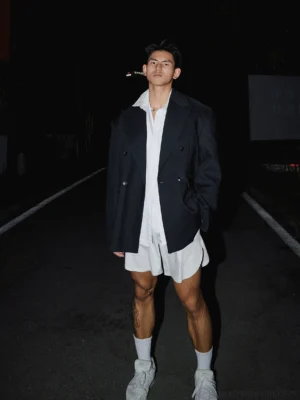 Full-body black oversized double-breasted blazer outfit with grid shirt, shorts, white socks and sneakers on an urban night street