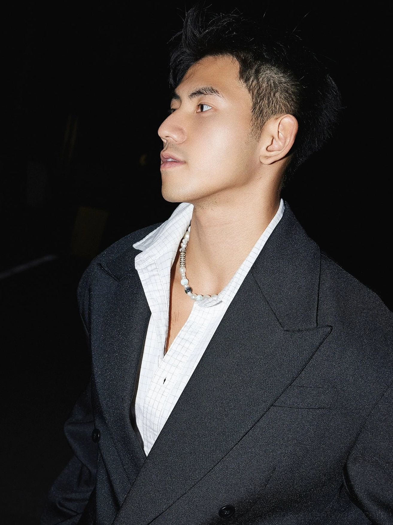 Side profile of black oversized double-breasted blazer showing structured shoulders, relaxed tailoring and pearl necklace styling