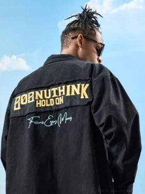 Black oversized embroidered button-up shirt shown from the back with yellow and white frayed patch embroidery and handwritten slogan
