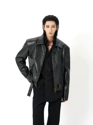 Black oversized faux leather moto jacket shown from a three-quarter front view with notch lapel, bronze zipper hardware, decorative studs, and adjustable waist buckle