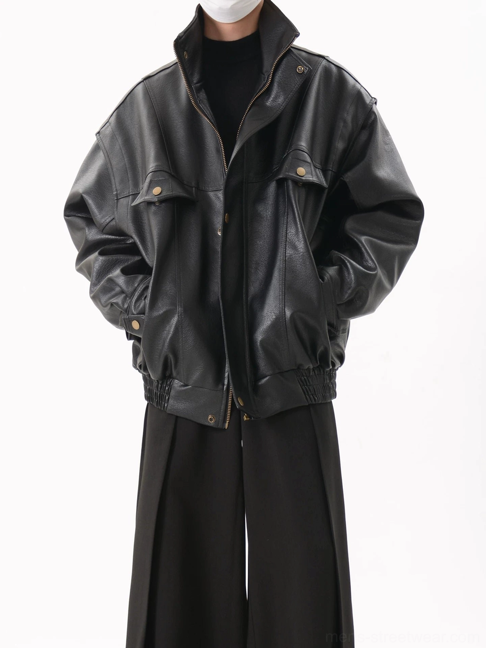 Three-quarter front view of a black oversized faux leather utility bomber jacket with dropped shoulders, high stand collar, flap chest pockets, antique-tone snap buttons, elasticated hem, and matte streetwear finish