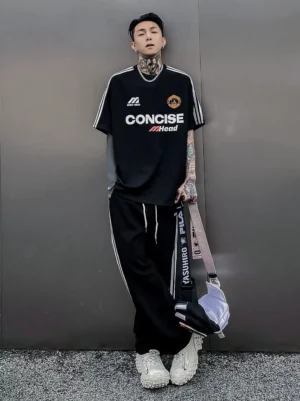 Black oversized football jersey-style streetwear T-shirt with contrasting white sleeve stripes styled with a crossbody bag