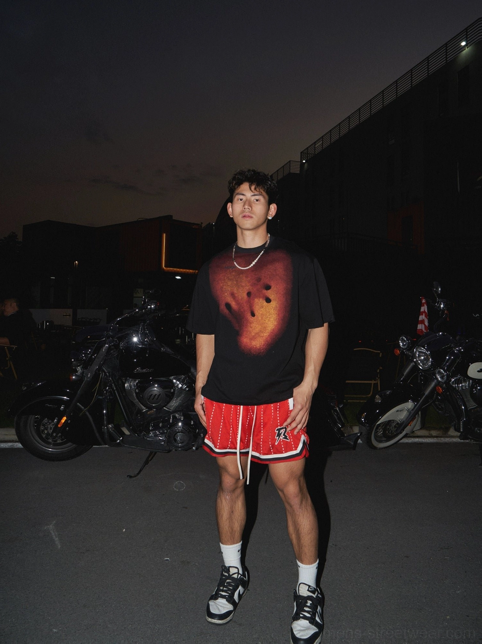 Black oversized graphic T-shirt styled with red striped basketball shorts skate shoes and white socks in an urban streetwear outfit