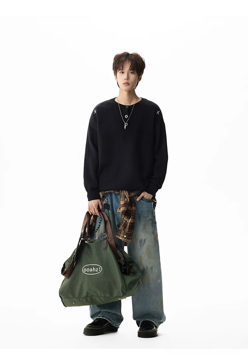 Full body styling of a solid black oversized henley knit sweater with a plaid shirt tied at the waist and canvas tote bag