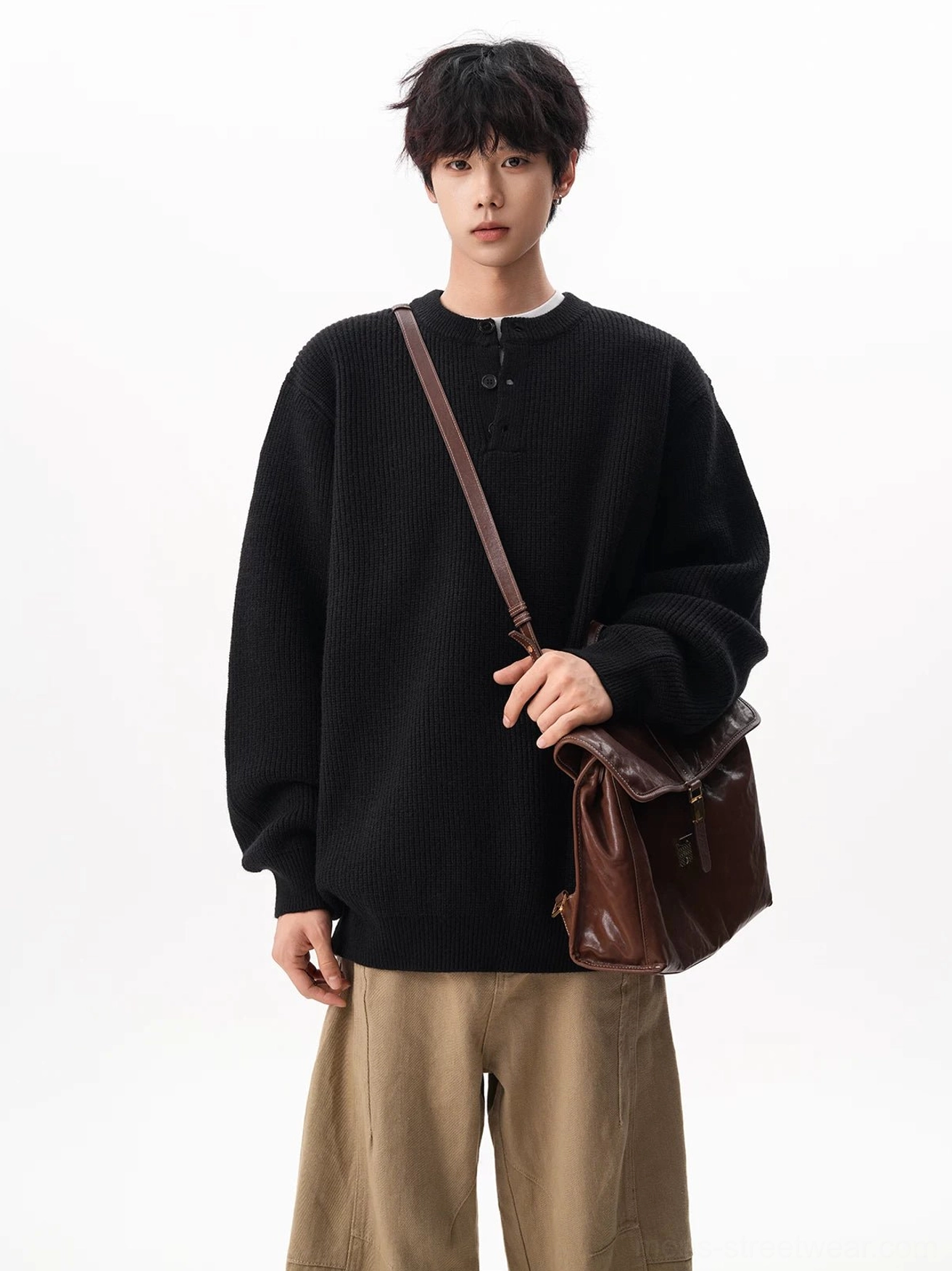 Black oversized Henley sweater with ribbed waffle texture styled with khaki trousers and a brown leather crossbody bag