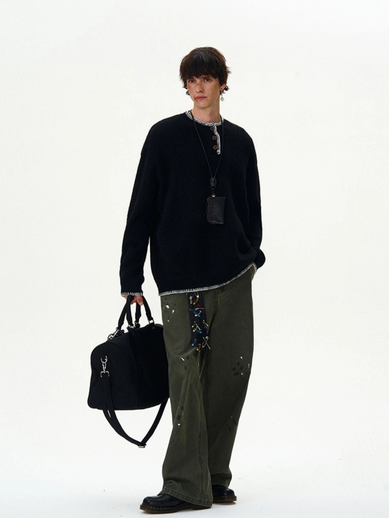 Full-body black oversized knit sweater with white contrast stitching paired with distressed green cargo pants and utility bag