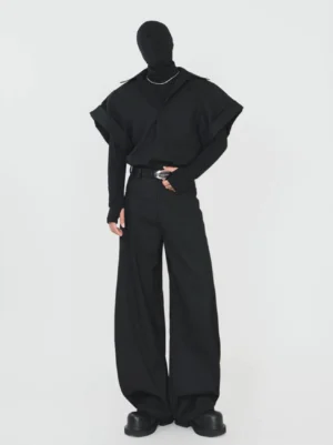 Full body view of a man wearing a black oversized layered shirt jacket with wide short sleeves, wide leg trousers, and silver buckle belt