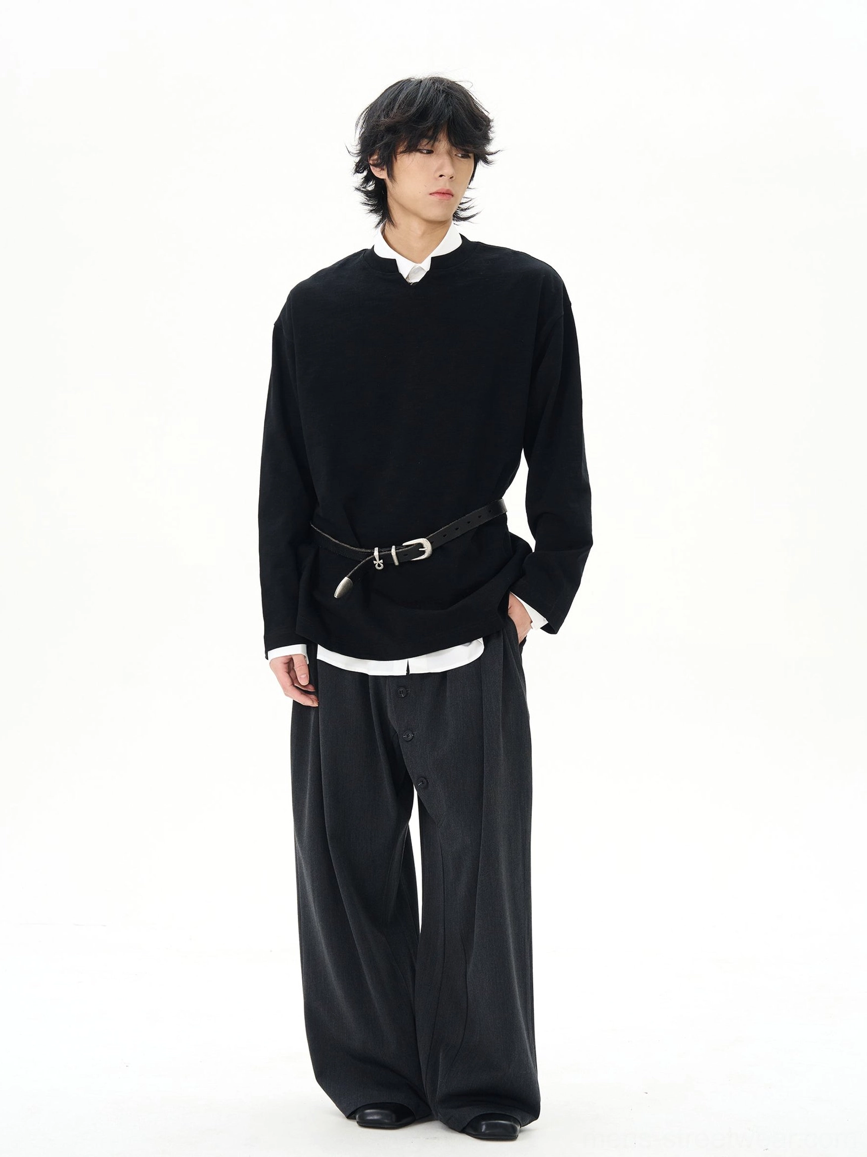Black oversized long-sleeve streetwear top styled with a layered white undershirt wide-leg black trousers and leather belt