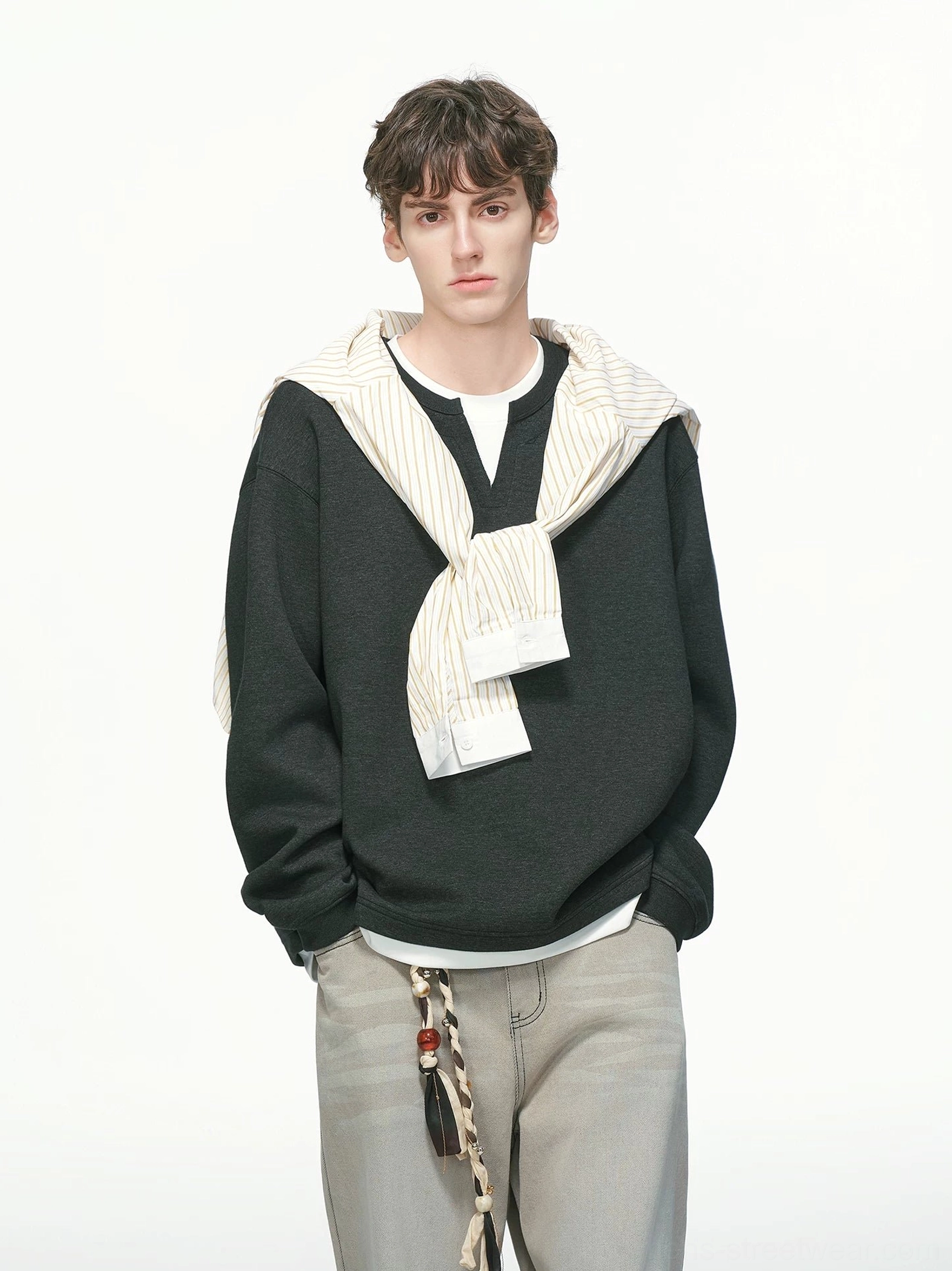 Black oversized layered crew neck sweatshirt for men shown from the front with white undershirt hem, khaki trousers, and casual streetwear styling