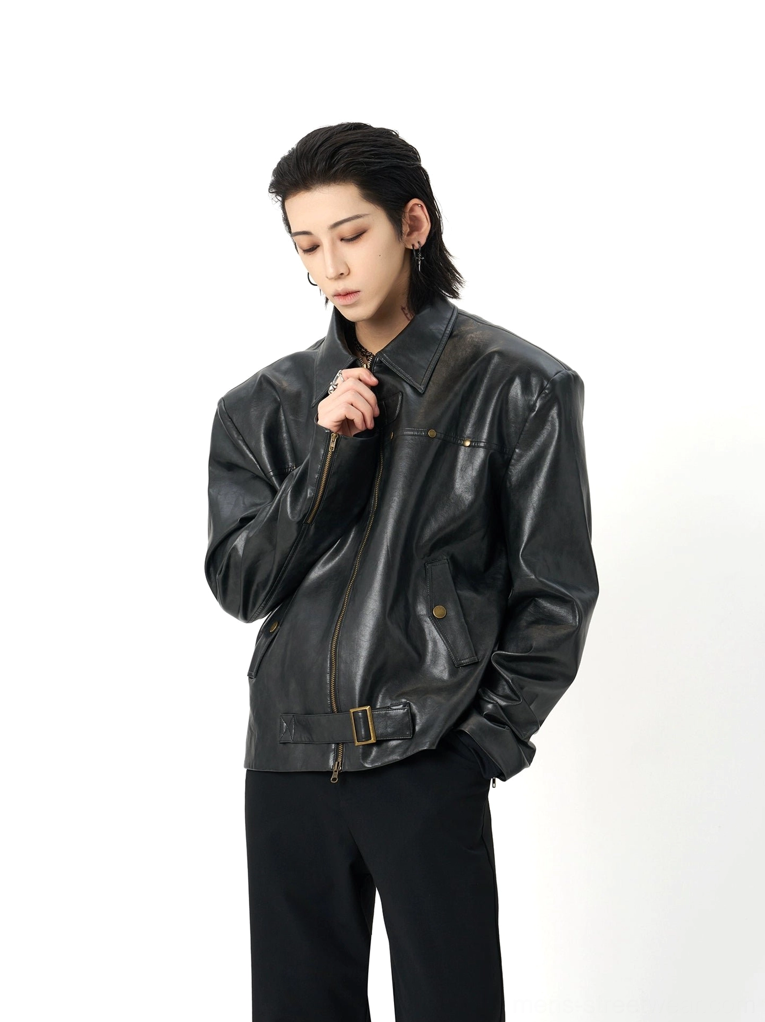 Side view of a black oversized moto leather jacket with front zipper, adjustable bronze waist buckle, notch lapel, and flap side pockets
