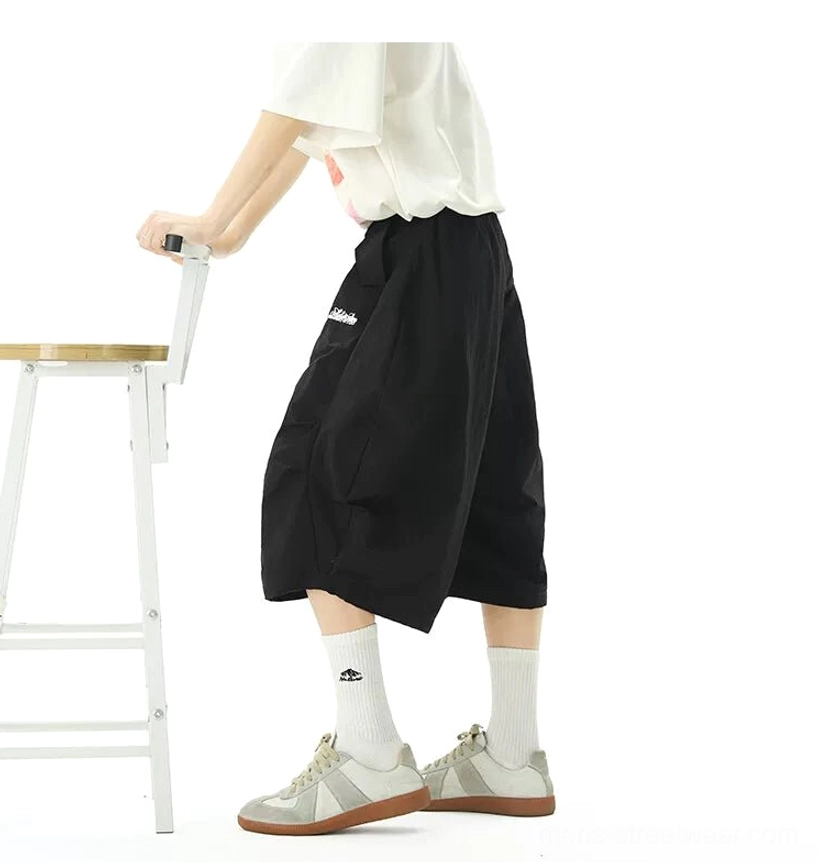 Rear side view of black oversized nylon jogger shorts showing wide balloon leg shape side pocket and cropped mid-calf hem