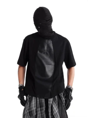 Close-up rear view of a black oversized patchwork streetwear tee showing the smooth matte faux leather back panel and curved hem