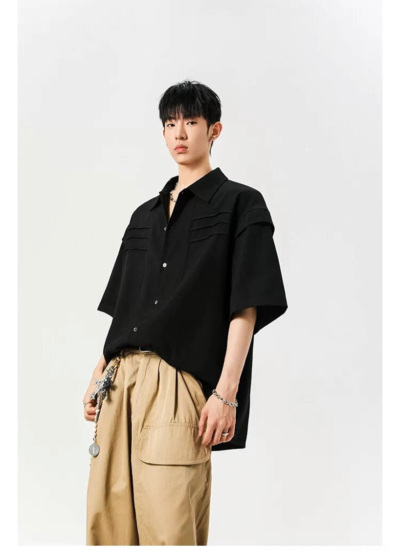 Black oversized pleated panel streetwear shirt shown from a side three-quarter angle with khaki trousers and chain accessory