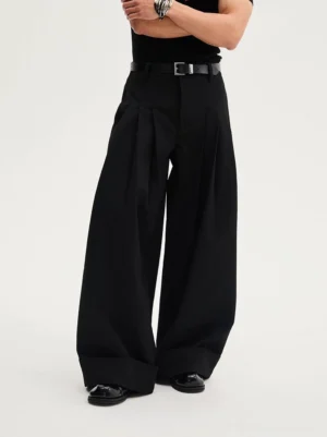 Black oversized pleated wide-leg trousers shown from a low front angle with tailored waist, rolled cuffs, leather belt styling, and dramatic Seoul streetwear silhouette