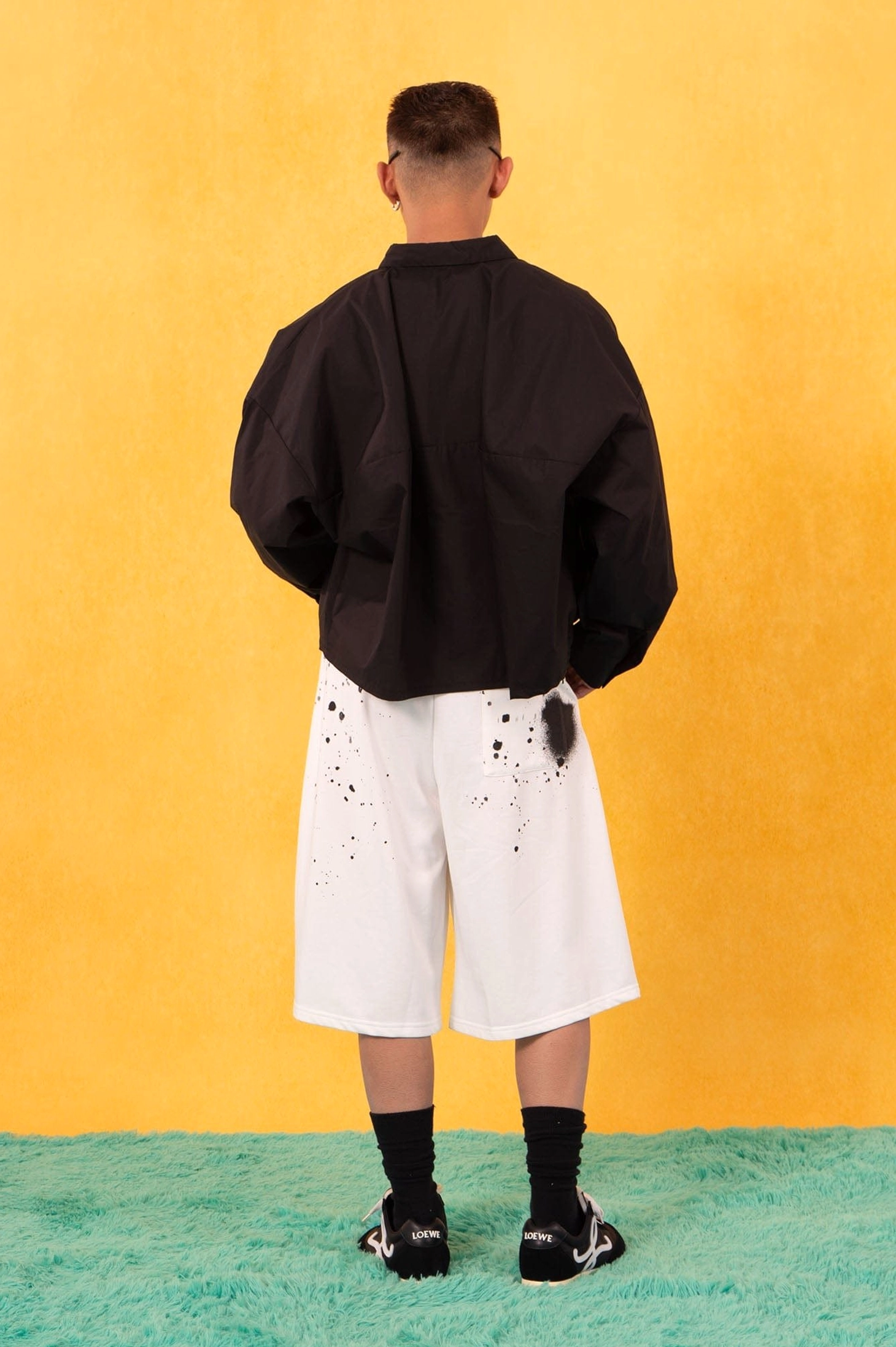 Back view of black oversized cropped poplin shirt paired with white splatter print shorts and a relaxed streetwear fit